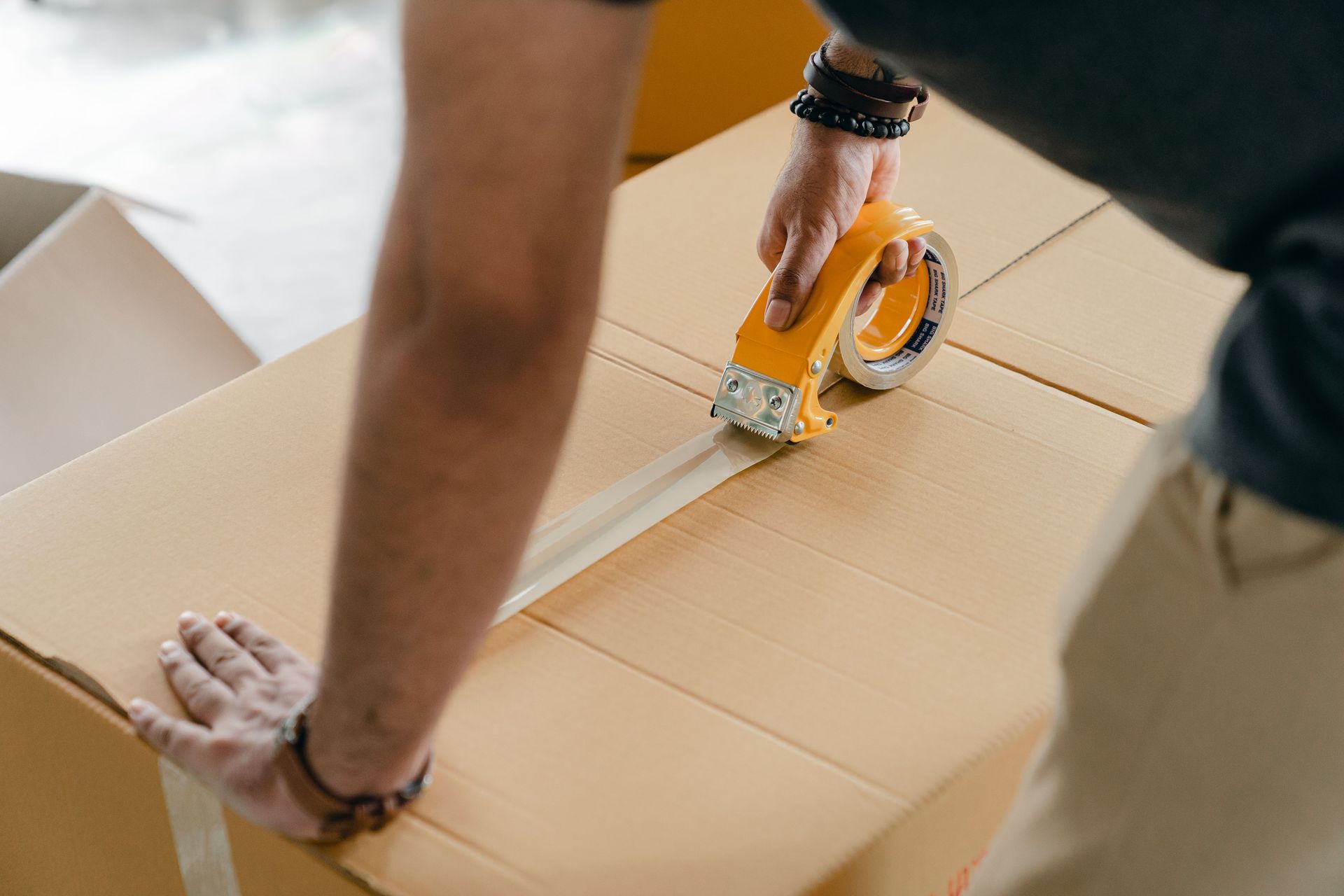 From above of crop anonymous young male using adhesive tape while sealing cardboard box