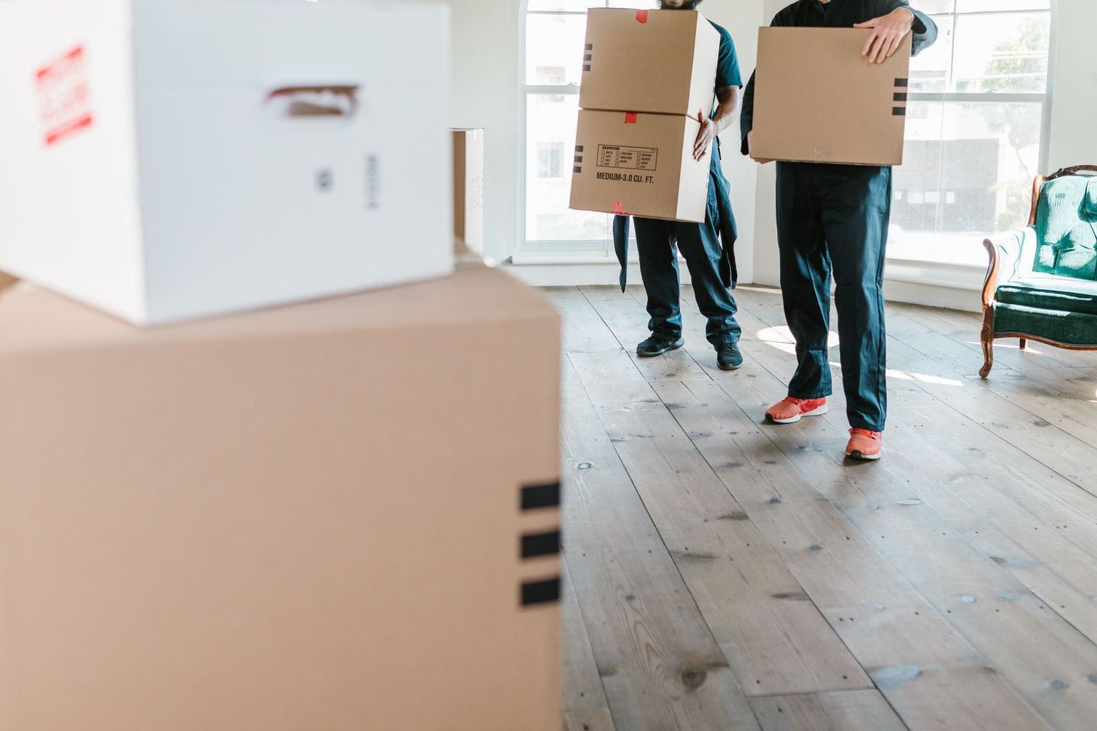 Two movers in uniform carrying boxes in a bright, new home setting.
