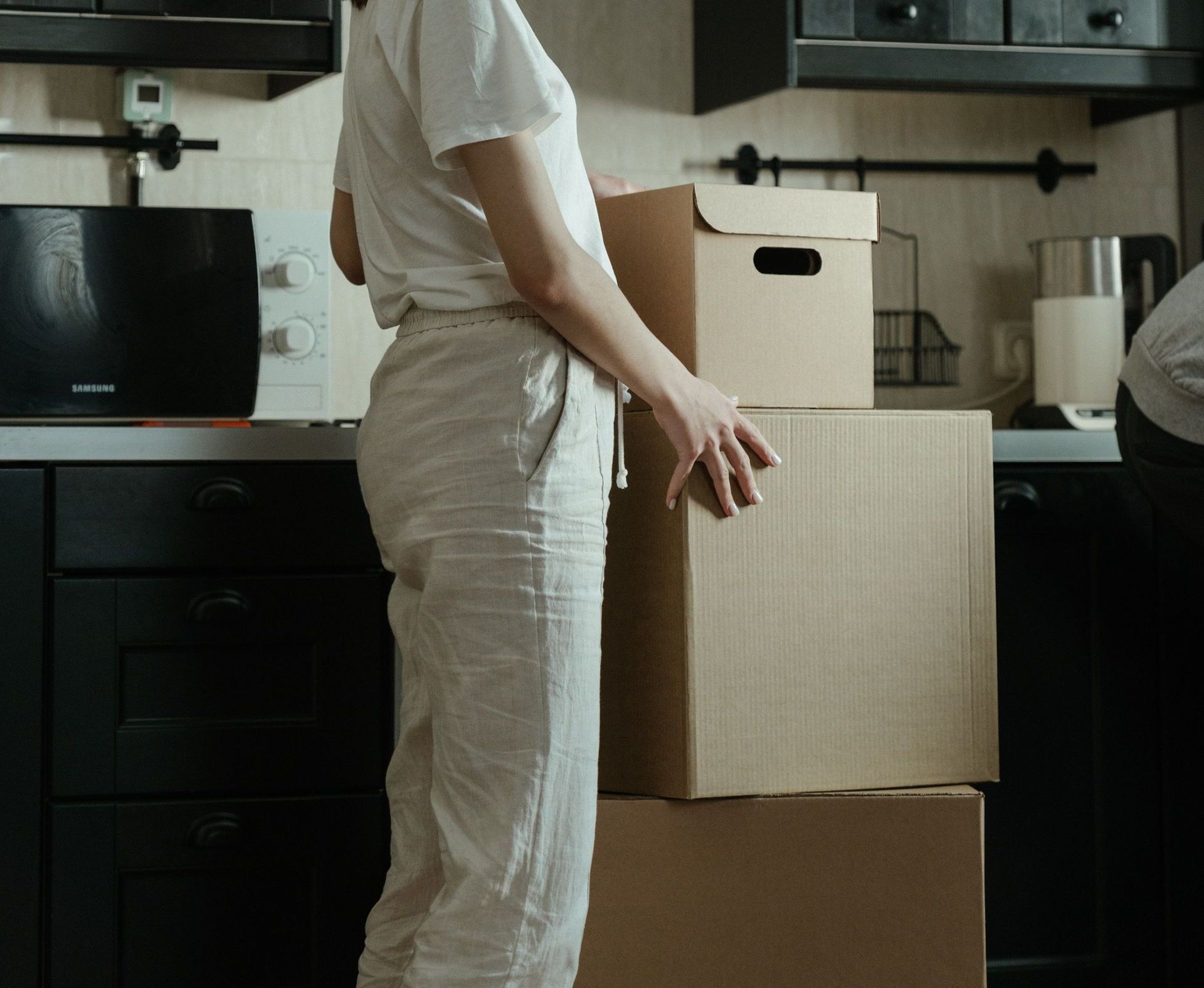 A woman standing in a kitchen unpacking cardboard boxes in a modern apartment.