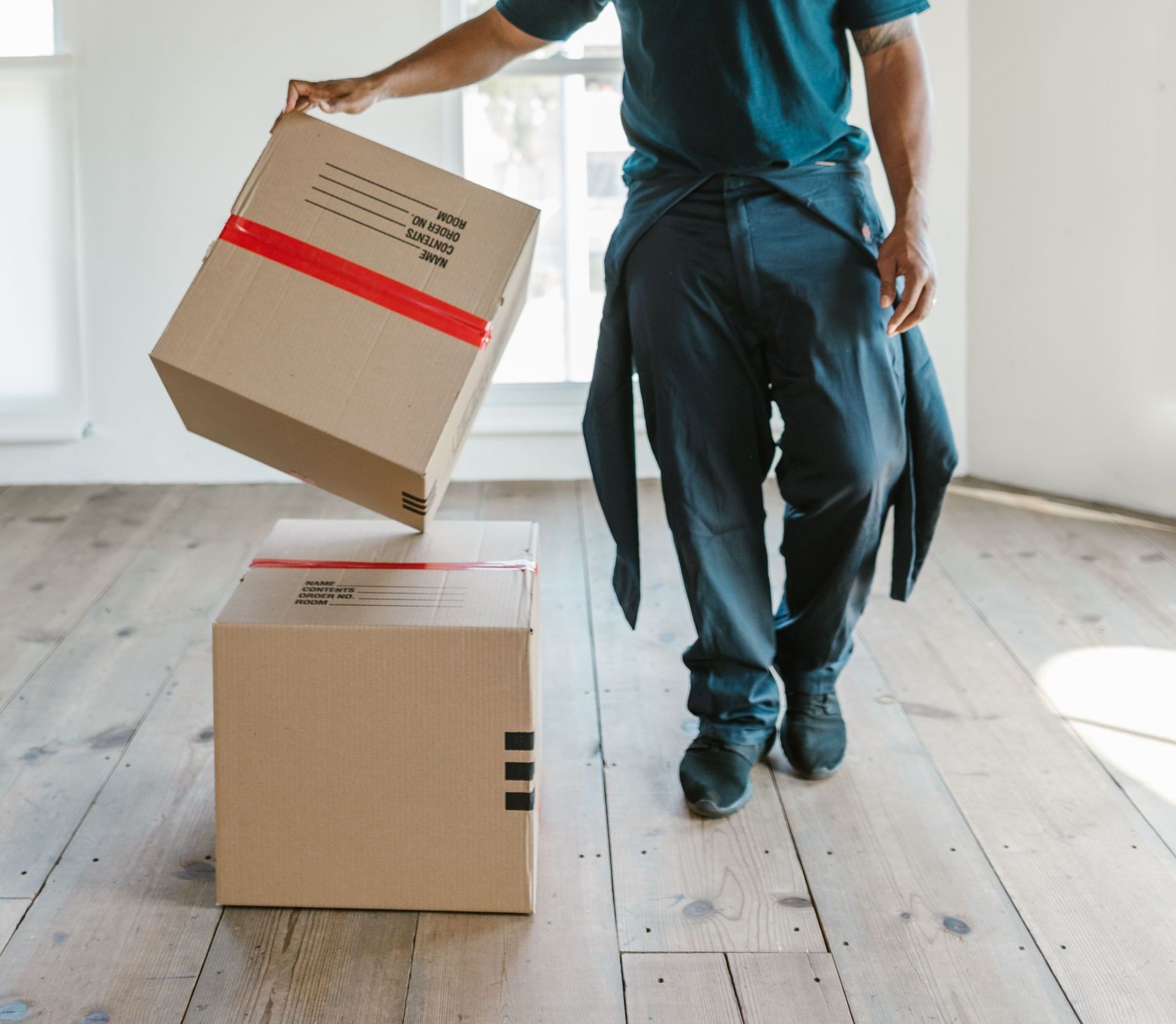 A mover carefully handles boxes in a bright, empty room on moving day.